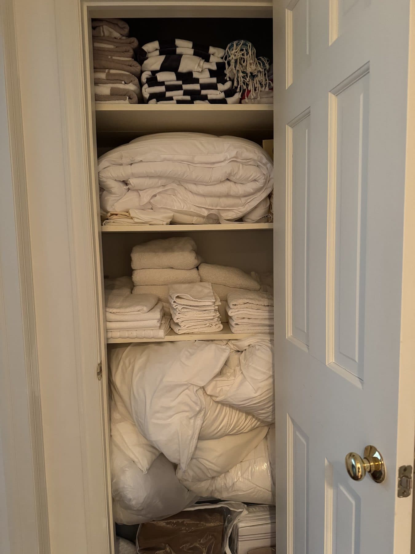 Linen closet with piled blankets before folding and organizing